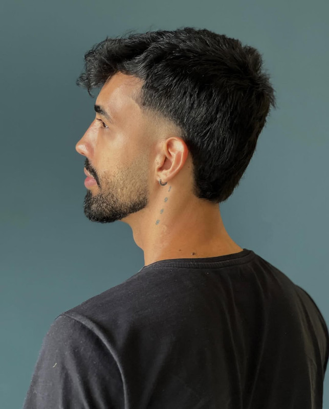 Corte de cabelo com finalização pompadour e barba cheia.